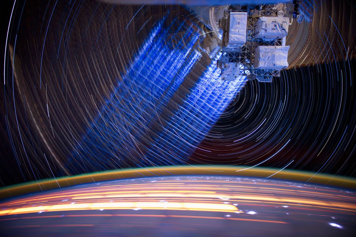 A long-exposure photo shows the trails of Earth and stars moving around the International Space Station.