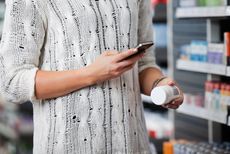 A woman shopping for medicine consults her smartphone.