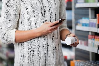 A woman shopping for medicine consults her smartphone.
