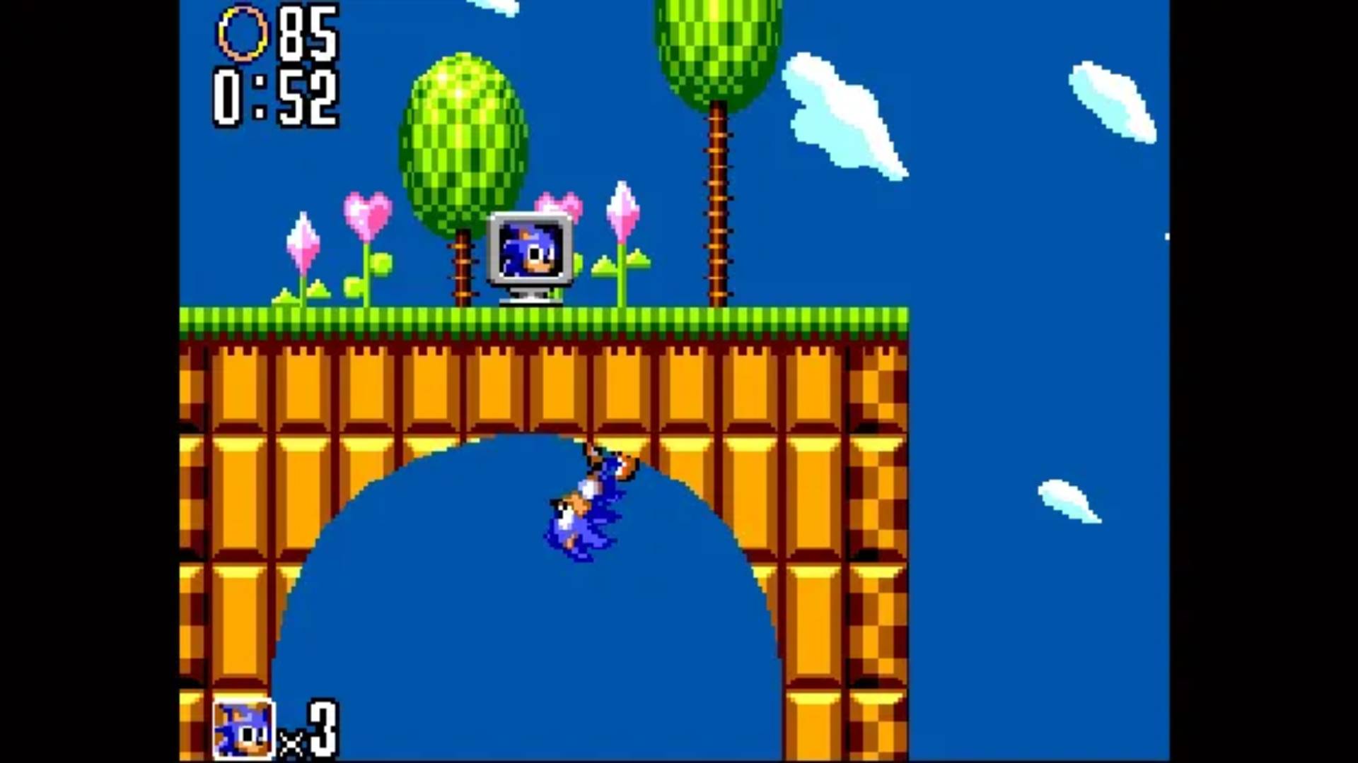 Sonic the Hedgehog screenshot of Sonic running through a loop, and a TV screen framed by trees with Sonic&#039;s face on can be seen on the grassy platform above