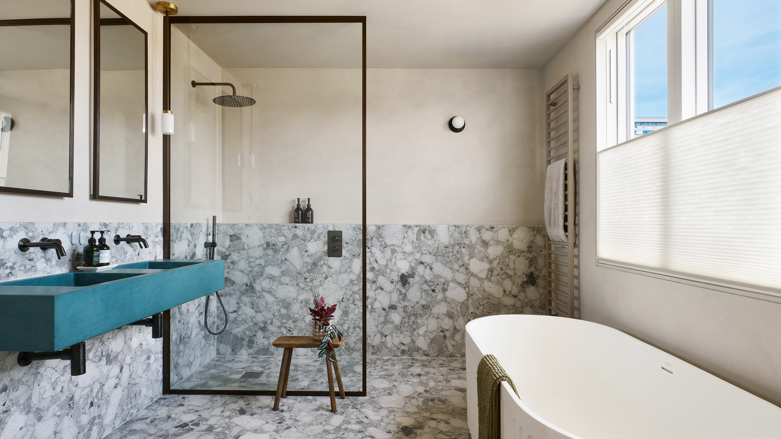 wet room with marble style flooring and walls with painted walls and blue double sink and white bath