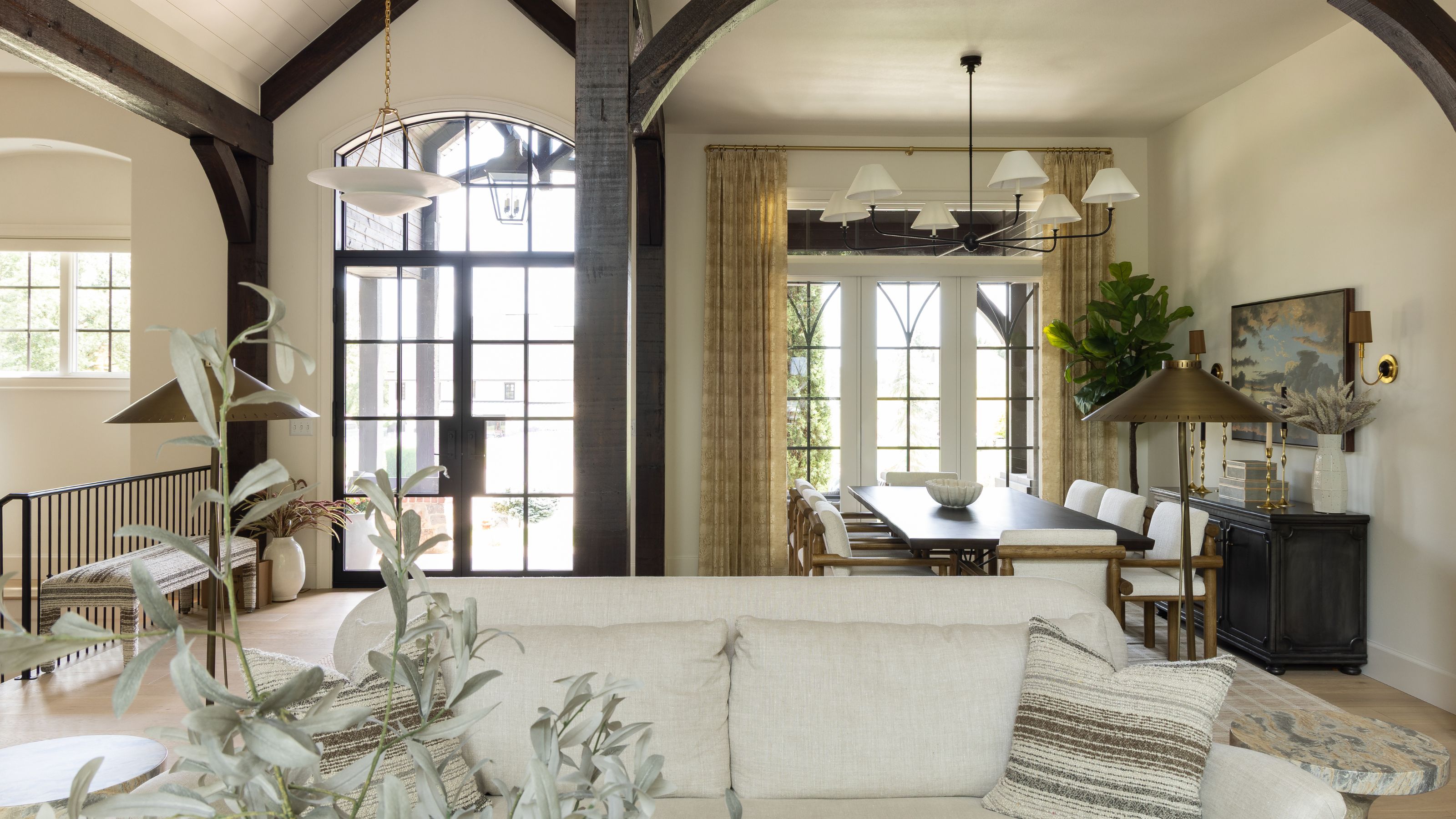 a light filled living and dining room area with large crittal doors and windows and dark wooden beams