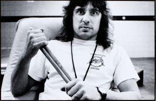 A portrait of Dave Lombardo holding drumsticks