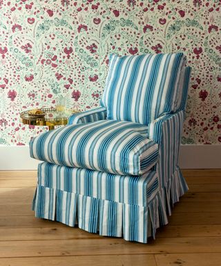Blue striped skirted chair in front of floral wallpaper