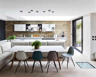 Open plan kitchen ideas illustrated in a large room with exposed brick wall and built-in dining room seating around a large table.