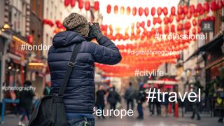 Person standing with the back to the camera, photographing a street scene, hashtags were added in the background