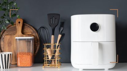 a dark grey kitchen with wooden counter with a white air fryer and utensils to show the best air fryer accessories for cooking