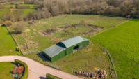 dutch style barn in a field with woodland to the back