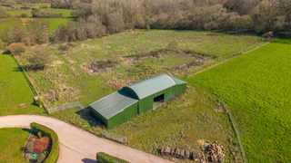 dutch style barn in a field with woodland to the back
