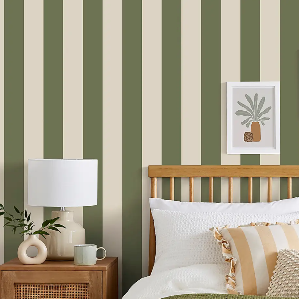Green and white stripe wallpaper behind a bed and bedside cabinet