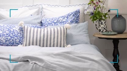 A close up photo of a bed with white breathable cotton bedlinen to show how to keep a bed cool in summer with blue floral cushions