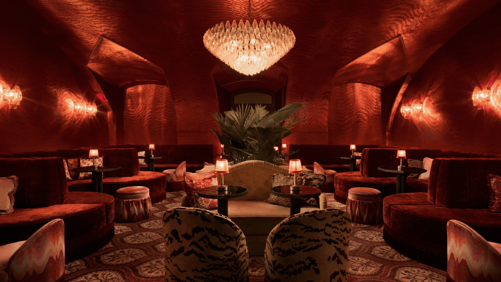 A rotating gif showcasing the plush, velvety red, leopard-print, and gradient-printed interiors of a glamorous cocktail bar with a retro soul and dimly lit lighting.