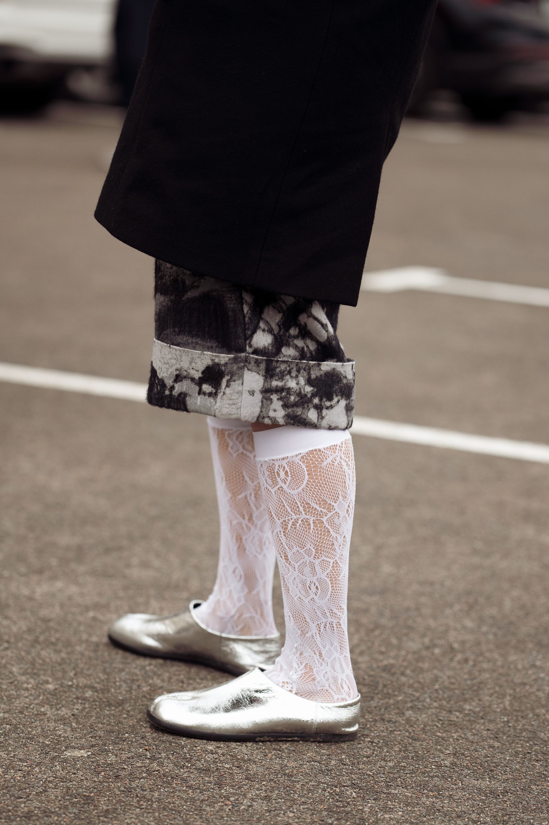 A woman wearing silver flats, white lace socks, and a black and white skirt