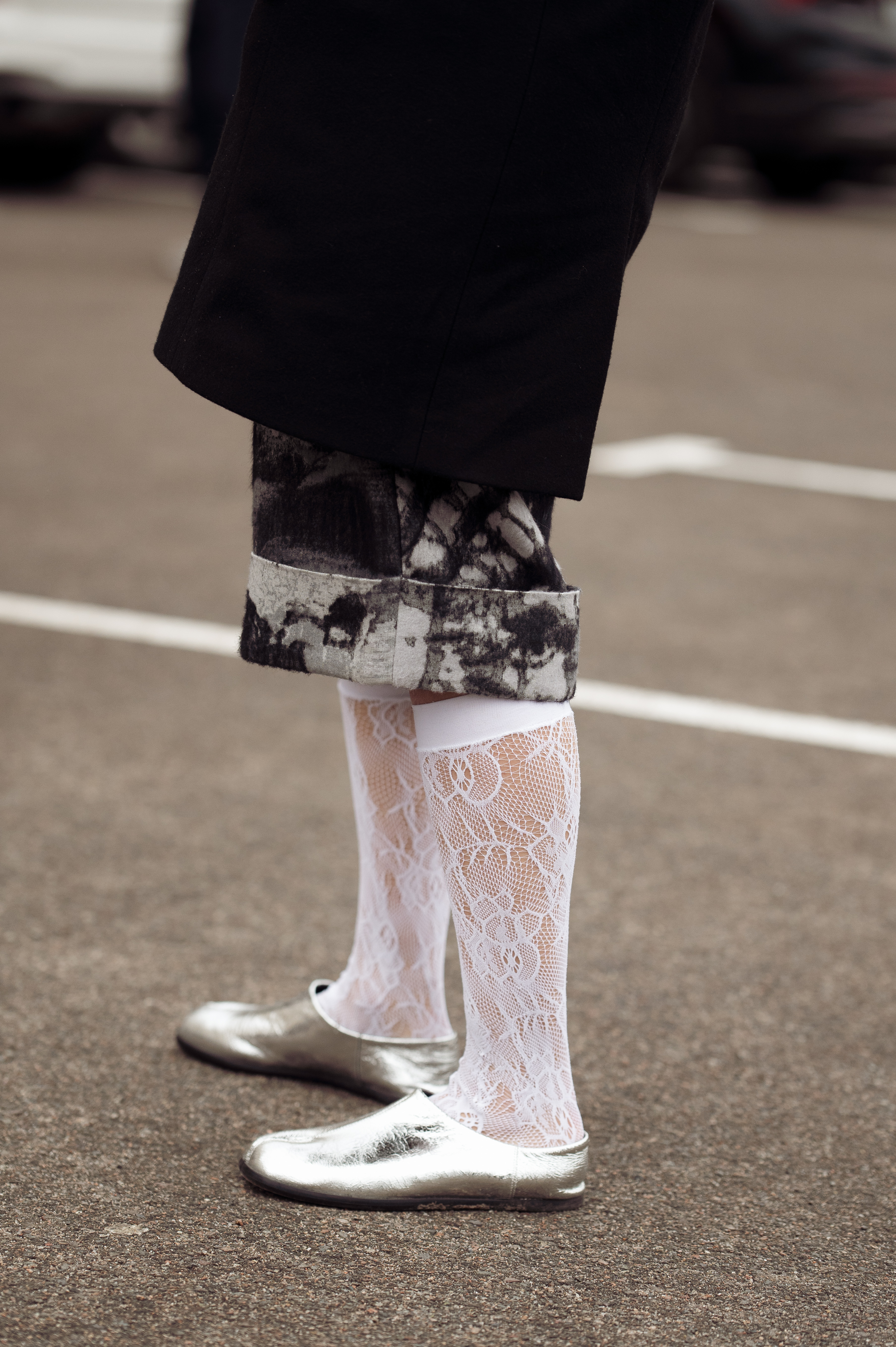 A woman wearing silver flats, white lace socks, and a black and white skirt