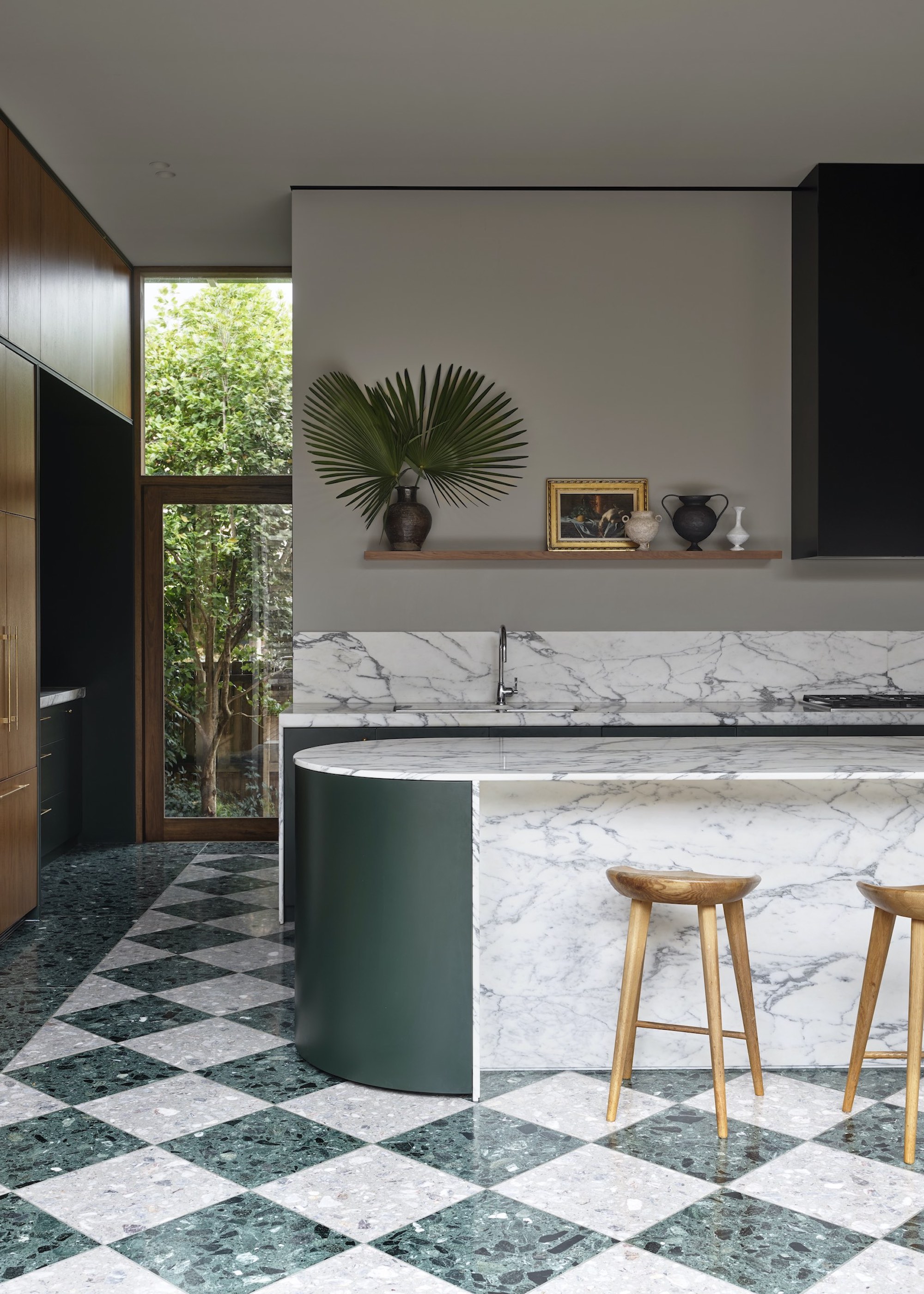 A kitchen extension with an island and chequered tile floor. The countertops of this kitchen are marble, and above the countertop is open shelving.