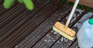 Wooden deck with a brush and cleaning solution to show how to clean decking