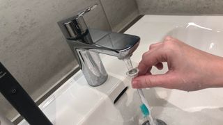 Electric toothbrush head being washed under a running tap