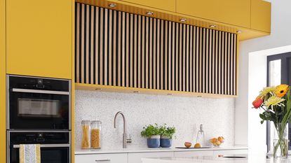 Yellow painted kitchen with wood panelling feature and white terrazzo tiles