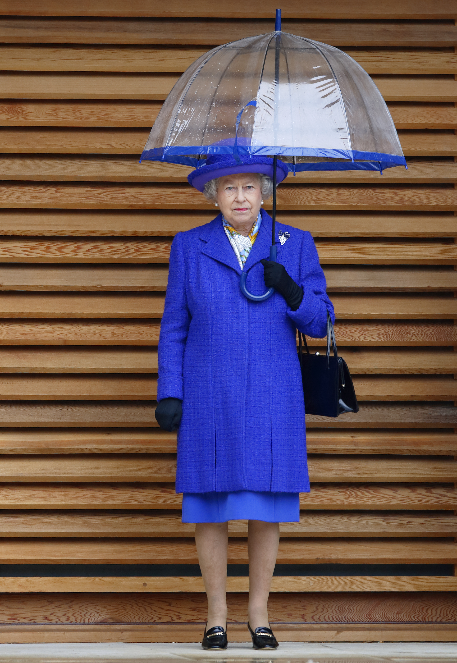 Queen Elizabeth in a bright blue coat holding an umbrella
