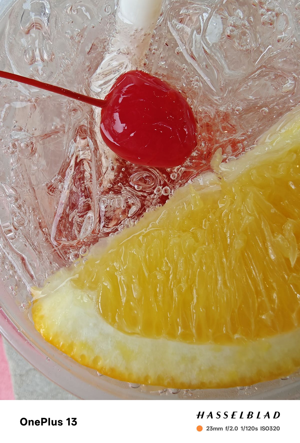 Close-up of an orange wedge and a cherry in a drink surrounded by ice and bubbles