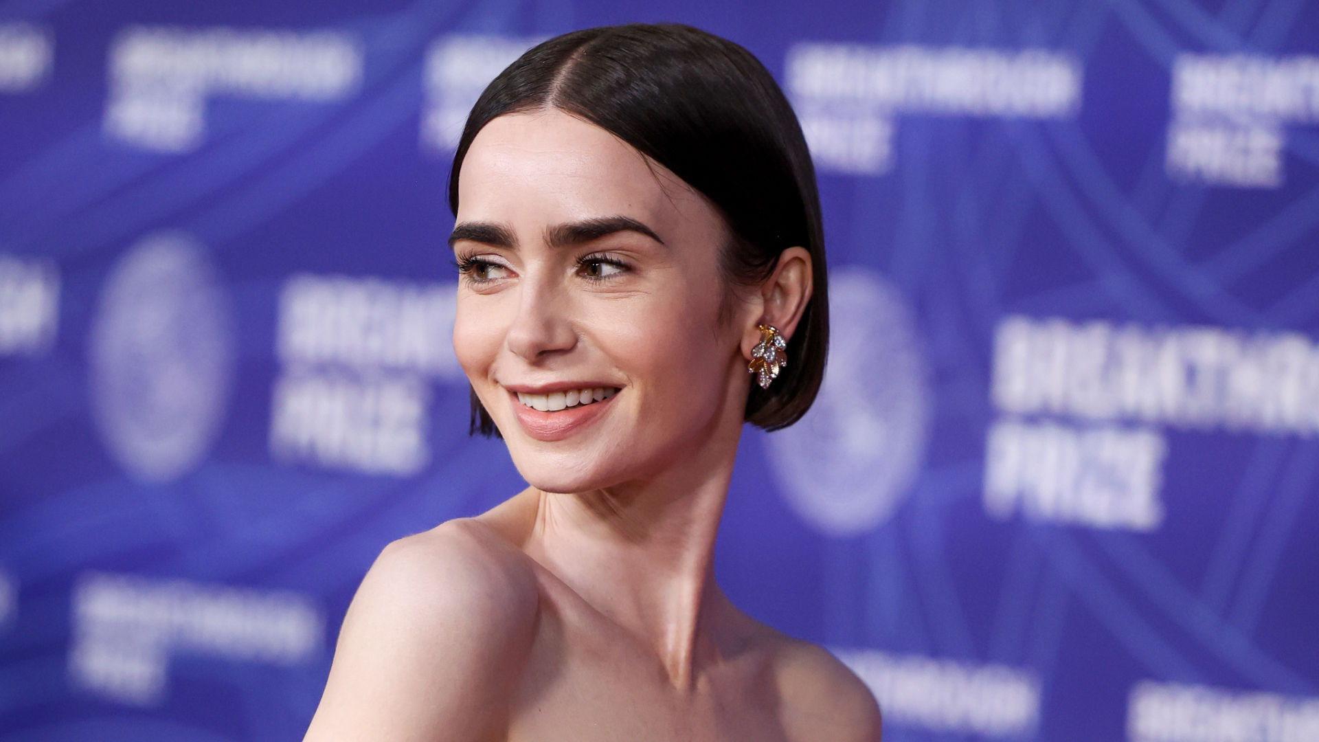 Lily Collins on a red carpet wearing a bob and diamond earrings