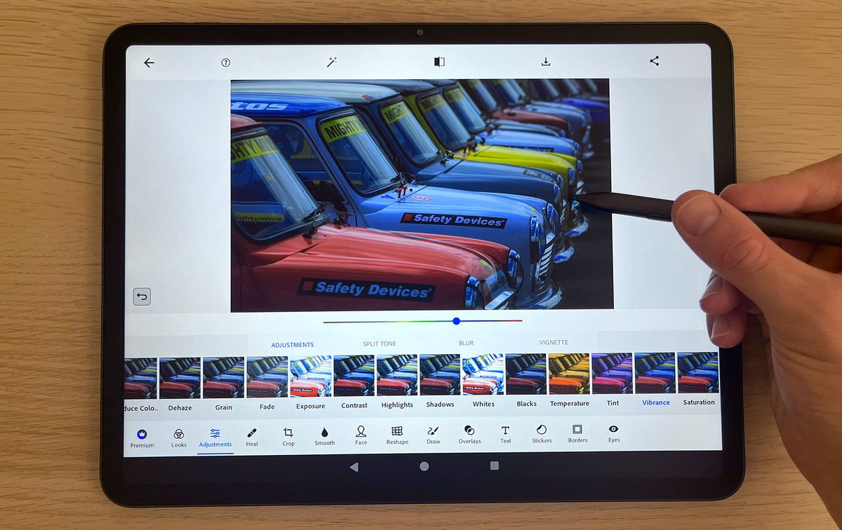 Hand using Huion Kamvas Slate 13 to edit image of cars on Adobe Photoshop Express