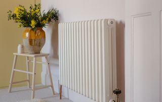 white radiator with stool and vase with flowers next to it