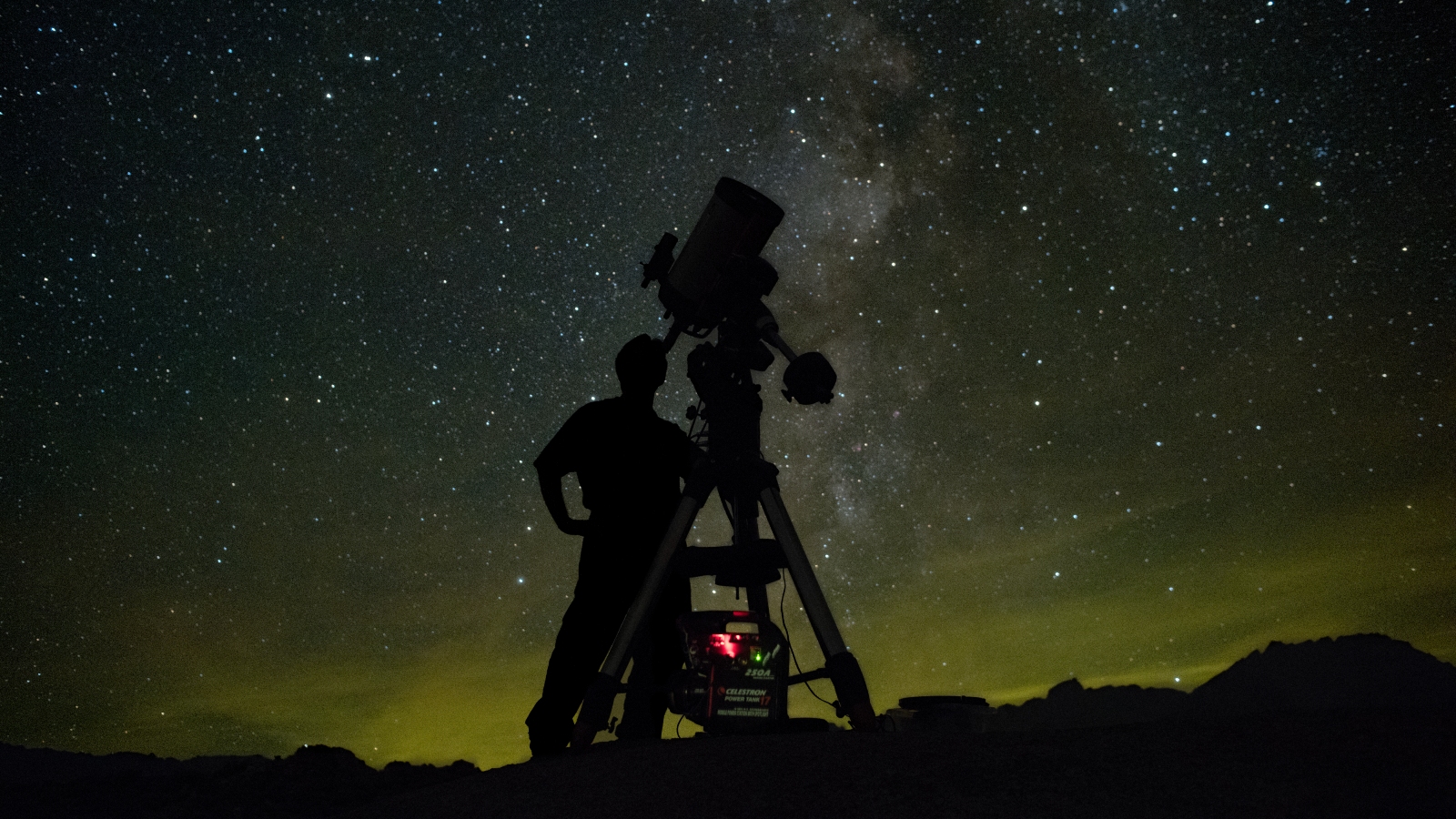 THe shadow of a man standing next to a telescope against a starry night sky