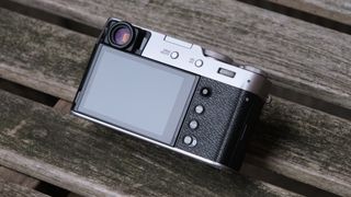 Fujifilm X100VI camera showing the screen and buttons, sat on on a slatted wooden bench
