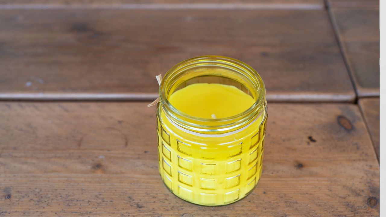 A citronella candle (unlit) placed on a wooden table