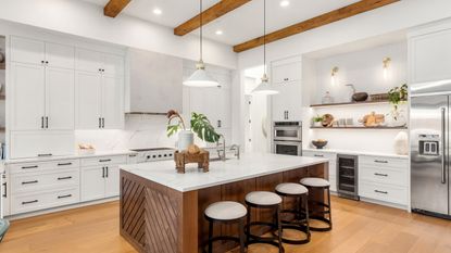 An image of a white kitchen with kitchen island in the foreground and white cabinets and countertops to the right 