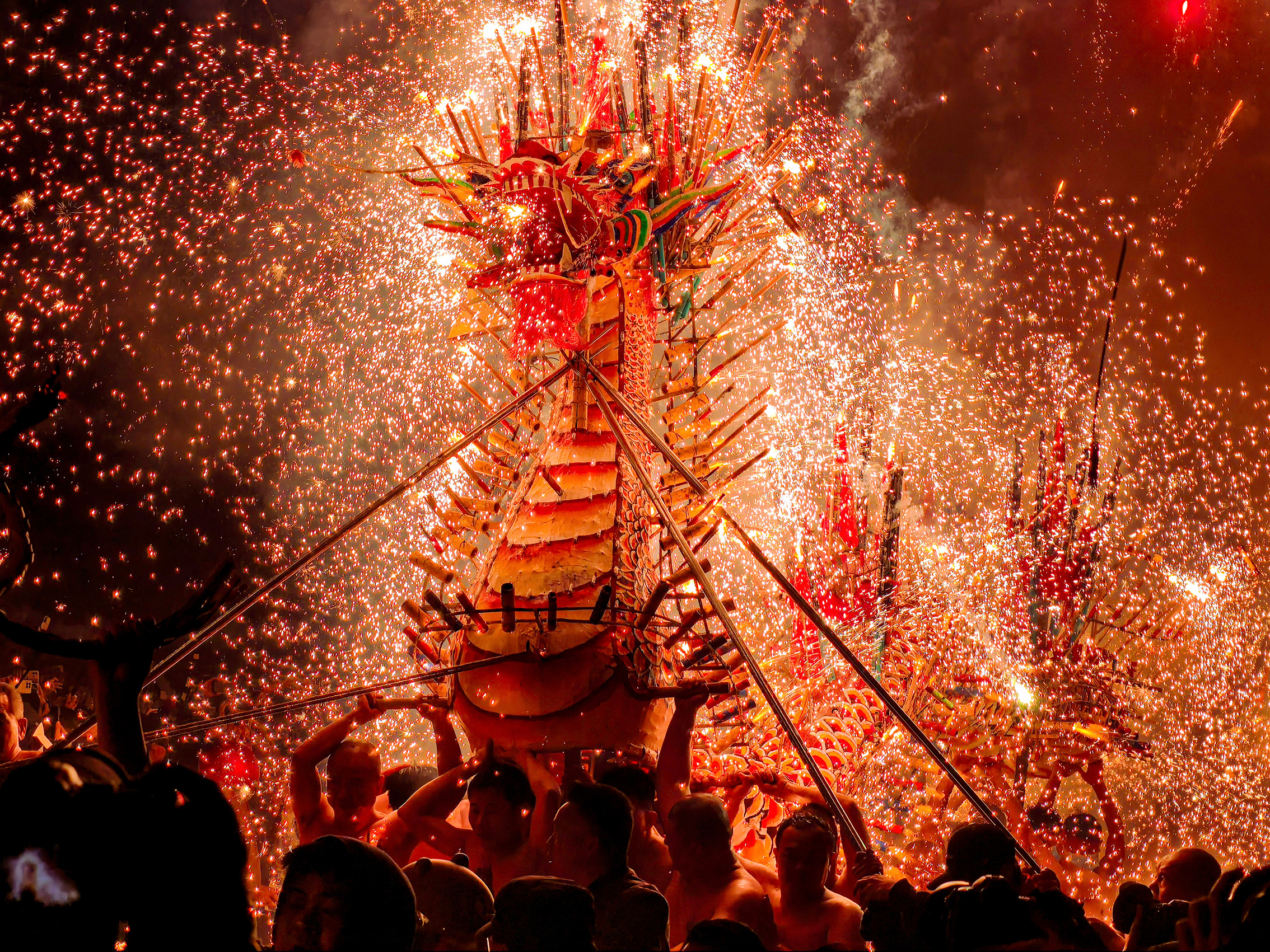 A vibrant dragon dance at a festival, surrounded by a shower of golden sparks from fireworks, people carry the dragon