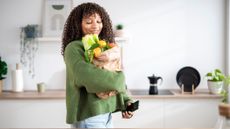 Woman holding brown paper bag of groceries in kitchen