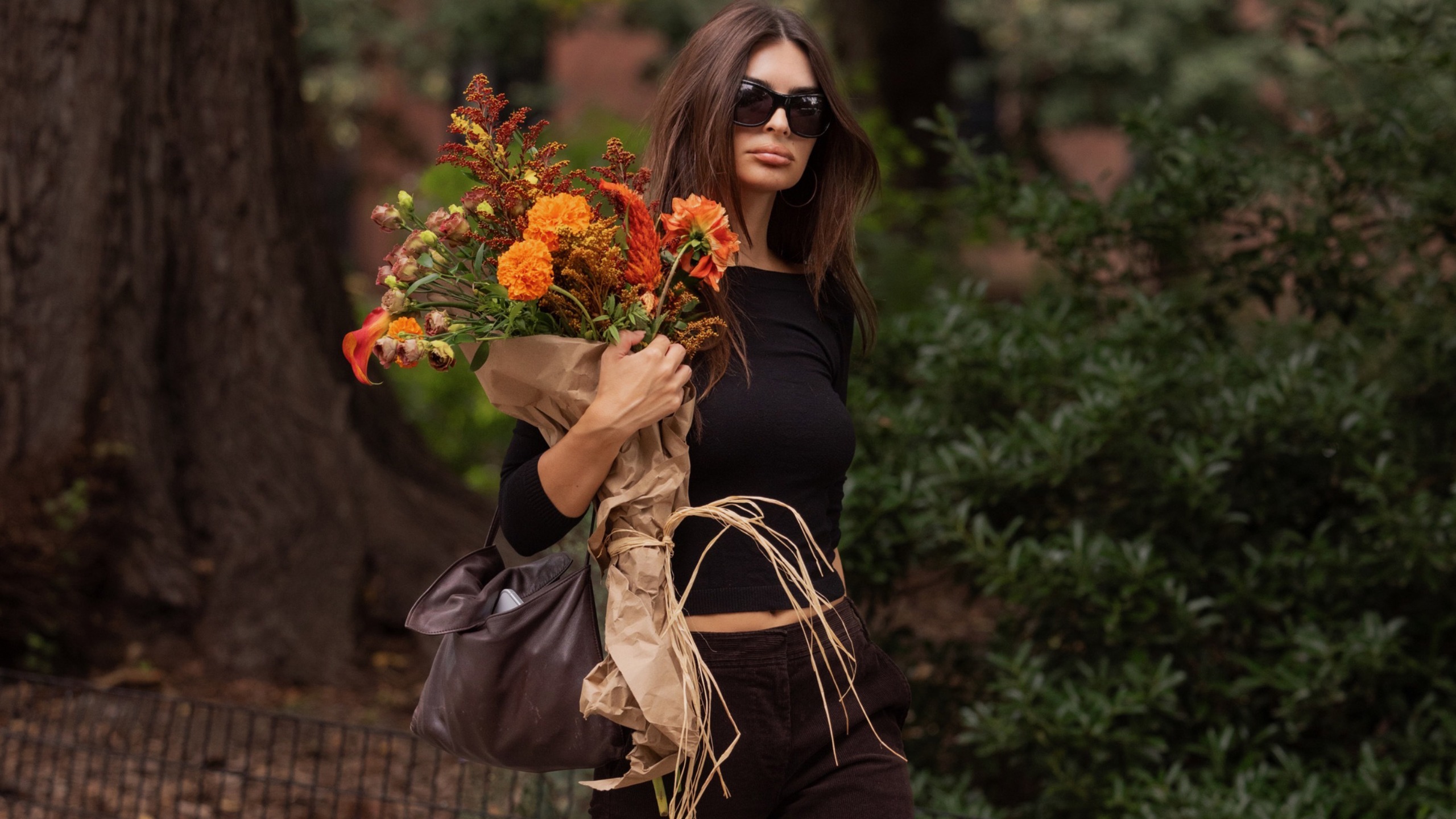 Emily Ratajkowski wears a long-sleeve shirt, oversized sunglasses and a brown leather bag.