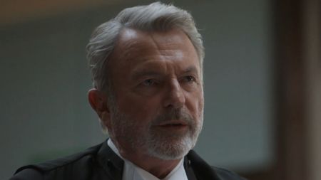 Sam Neill wears a suit on The Twelve while in a courtroom scene.