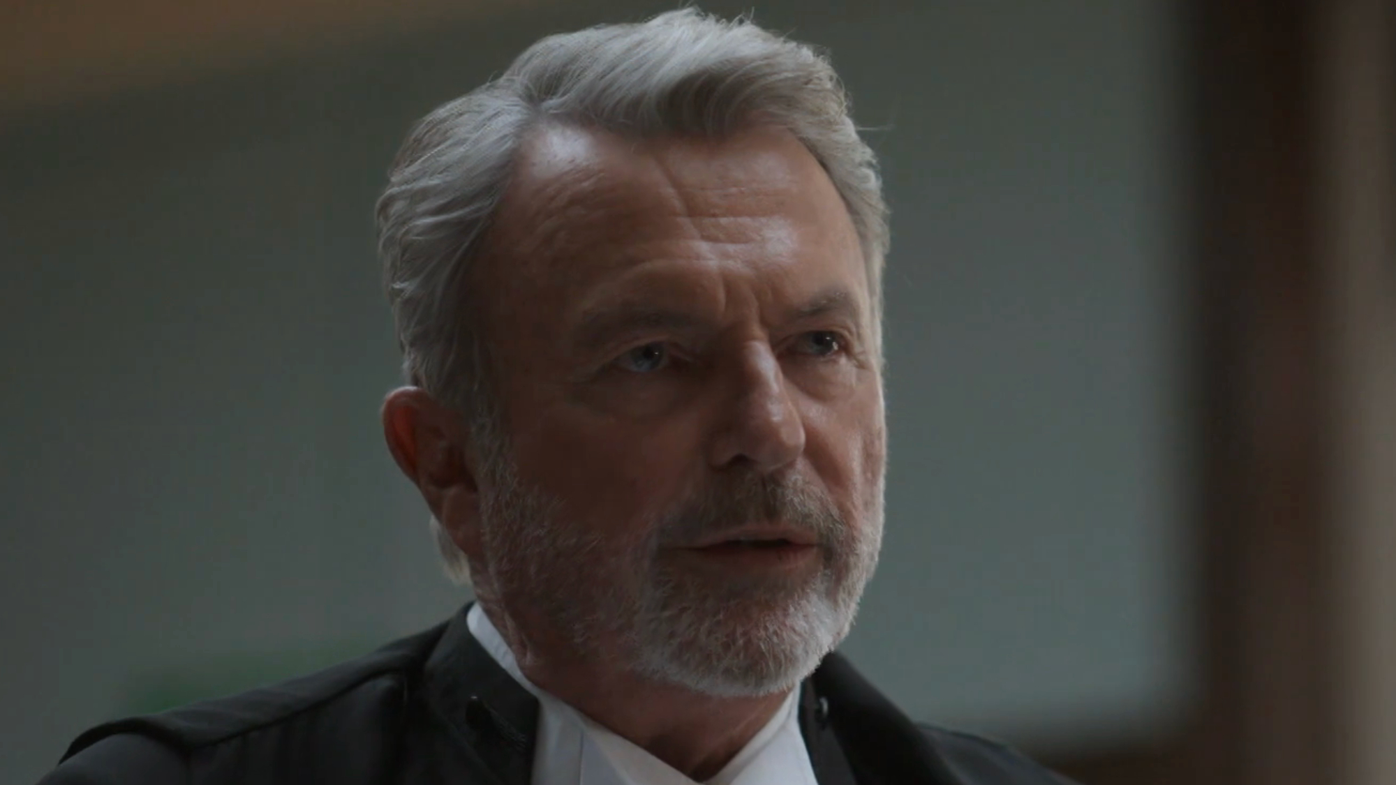 Sam Neill wears a suit on The Twelve while in a courtroom scene.
