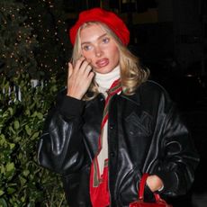 Elsa Hosk wearing a red beret, cream turtleneck, silk scarf, black leather bomber jacket, cream trousers, and black leather loafers to a Ralph Lauren event in Los Angeles