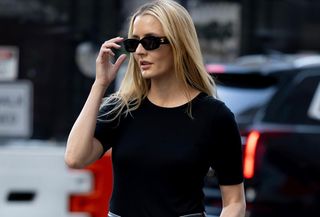 Woman wears black t-shirt, black belt, blue jeans, and black sunglasses.