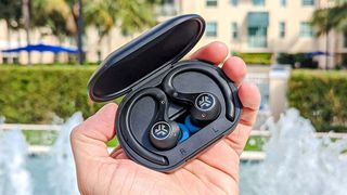 The JLab Epic Air Sport ANC (2nd Gen) wireless earbuds held in hand behind a fountain backdrop