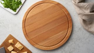 An empty wooden chopping board on a marble worktop, with a dish of fresh rocket leaves and another board of chopped parmesan pieces just visible