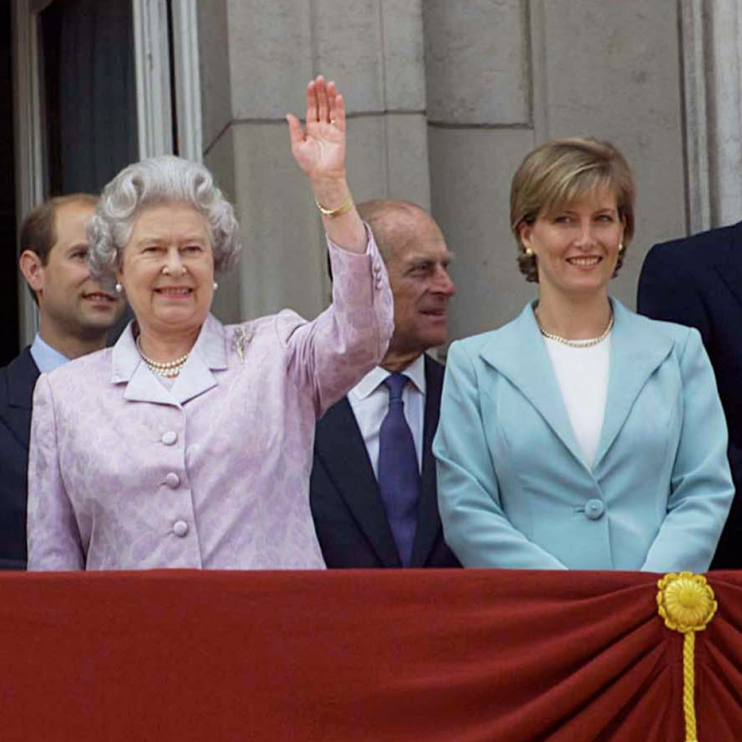 Queen Elizabeth wears a lilac and white suit and waves from the Buckingham Palace balcony while standing with Prince Edward's wife Duchess Sophie