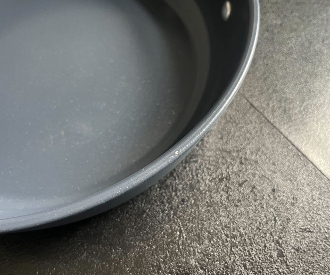 Slight peeling on the edge of a blue pan with a copper handle, on a black kitchen counter