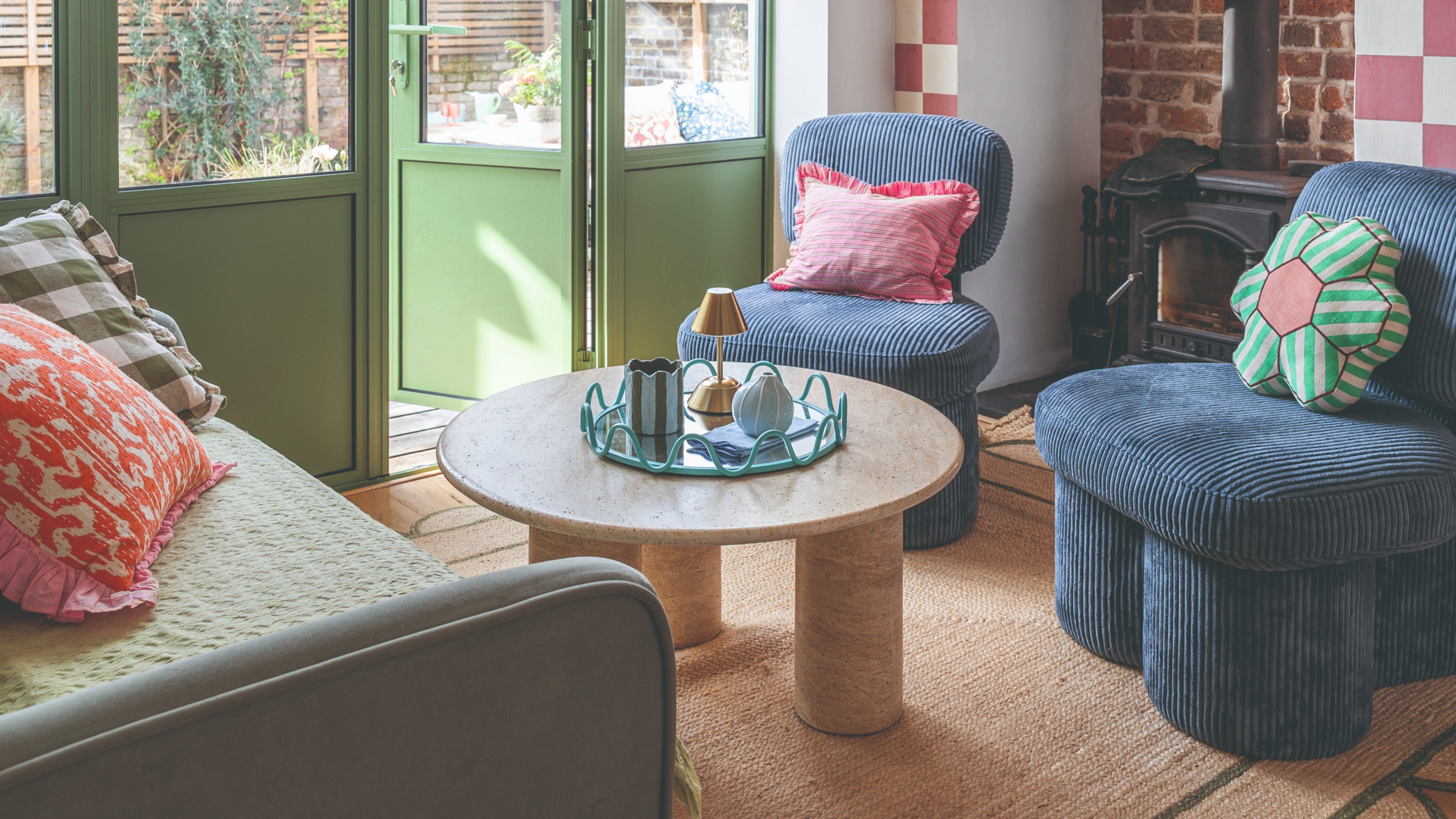 A small living room with a round marble coffee table, a green sofa and two blue corduroy accent chairs on a scalloped jute rug
