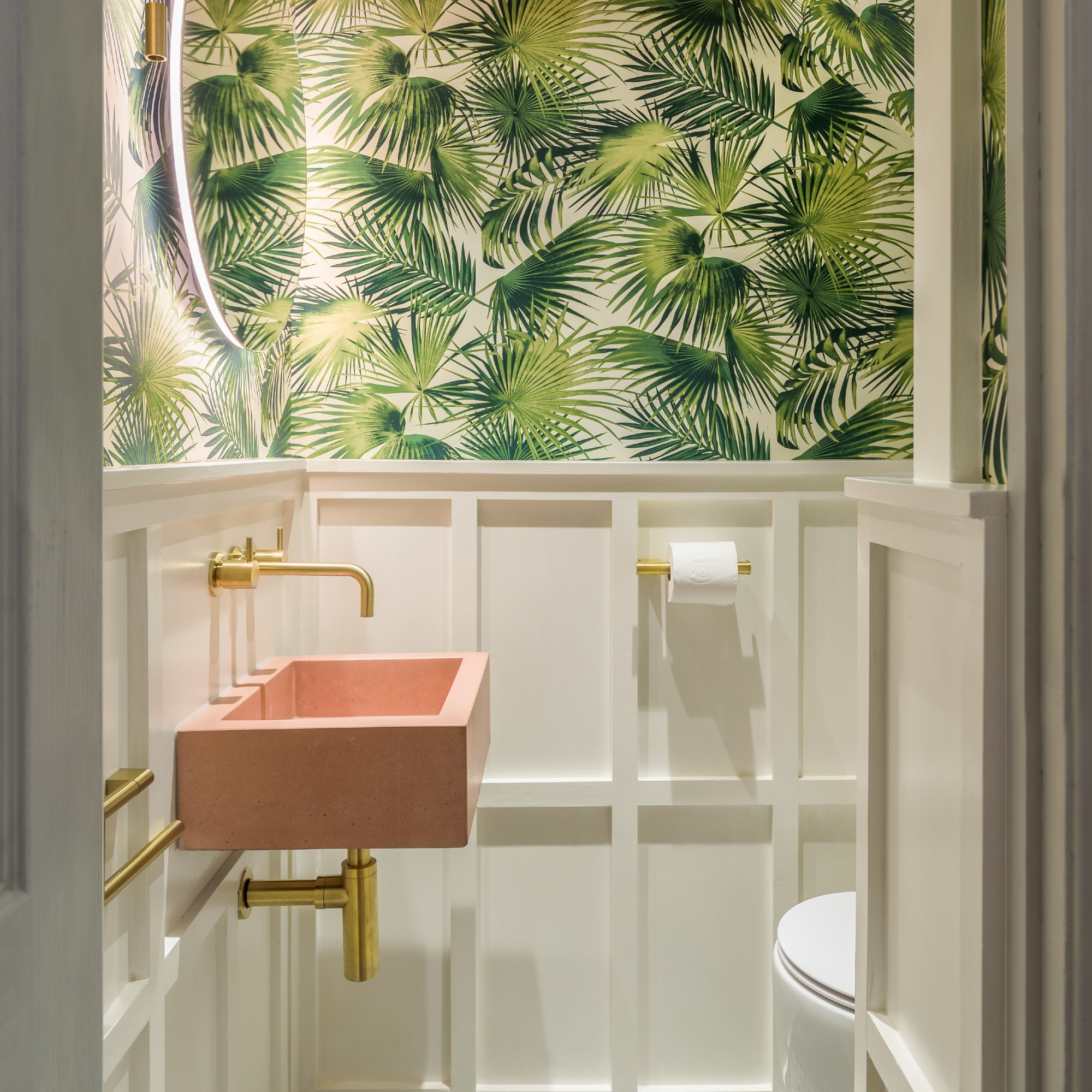 A cloakroom with a pink sink and a tropical wallpaper