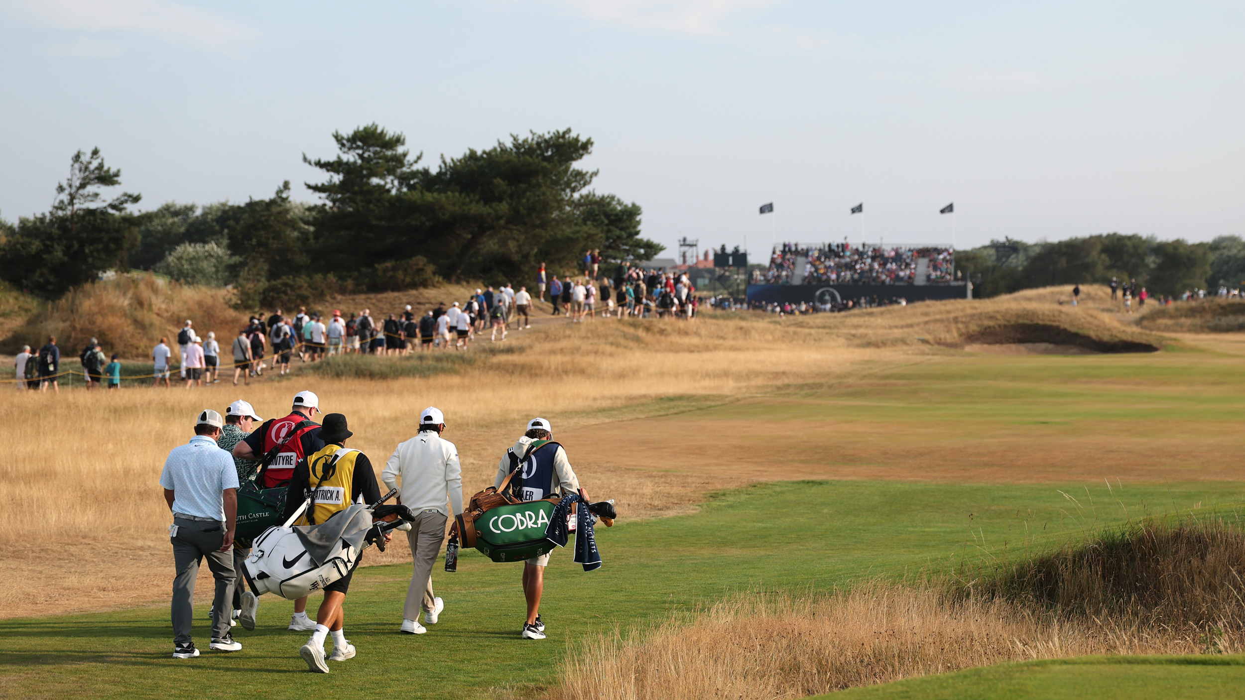 Players and caddies walk down a fairway at the 2026 Open