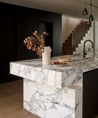 A marble kitchen island in front of a dark wall and staircase