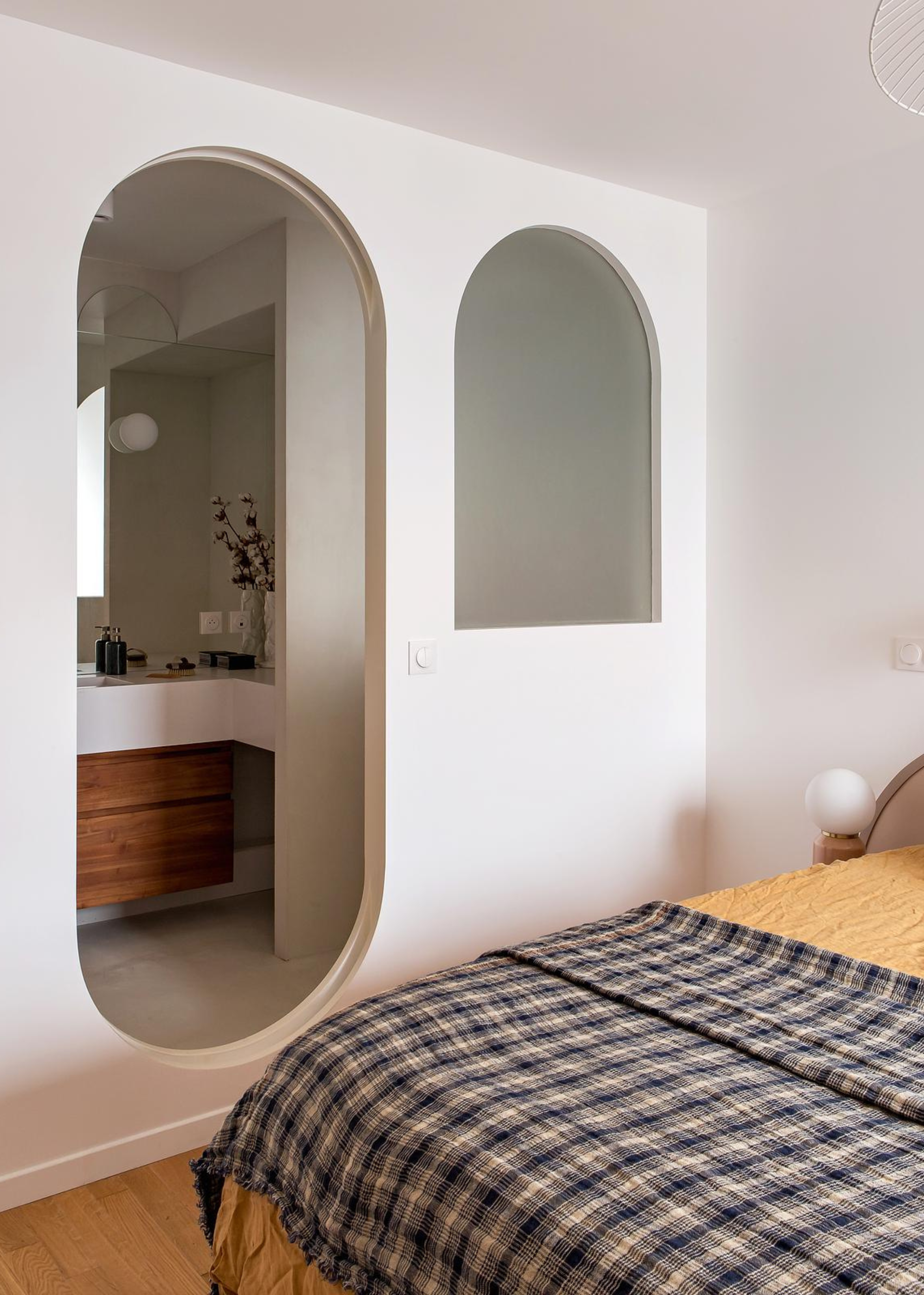 A tidy bedroom with a plaid throw, and a curved doorway leading to the bathroom