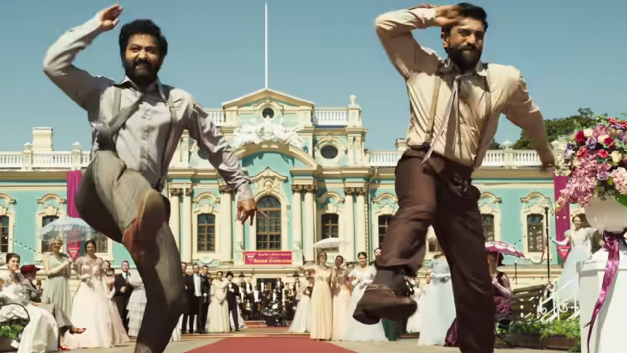 Two men dancing and raising their right arms in unison in RRR