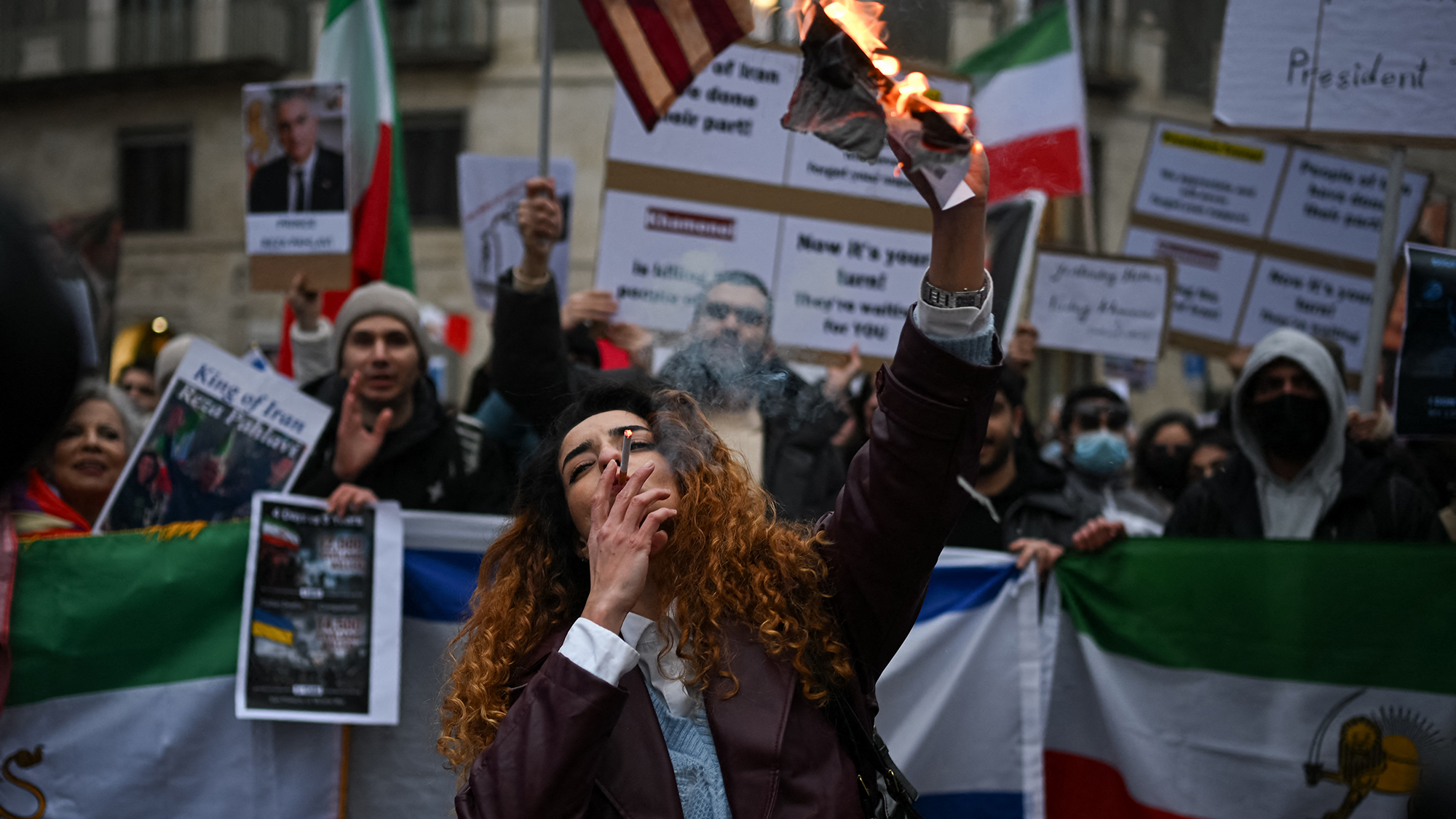 A protestor lights a cigarette with a burning image of Iran's supreme leader, Ali Khamenei, during a demonstration in Milan, Italy
