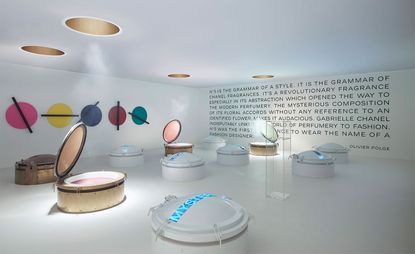View of the Chanel No.5 room at the Mademoiselle Privé exhibition featuring white floors, white walls with black text and colourful circles and circular visual displays to help visitors understand how Chanel No.5 perfume is made